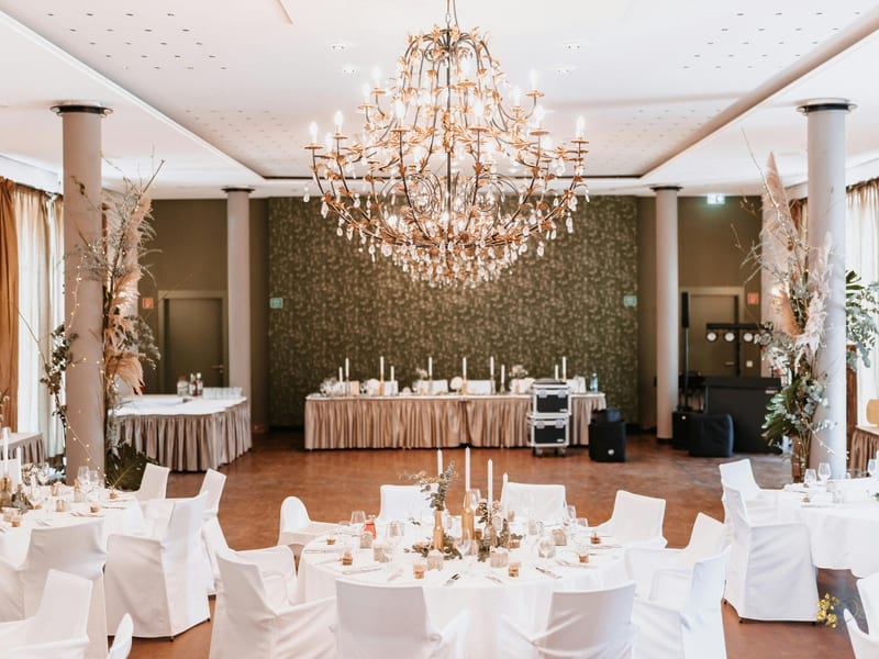 Elegancka sala weselna z kryształowym żyrandolem, kremowymi tkaninami i białymi stołami